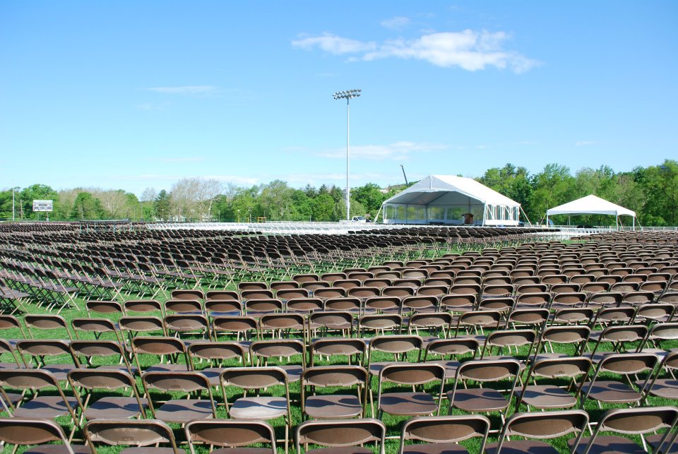 brown chairs on green lawn with tented stage for college campus event.