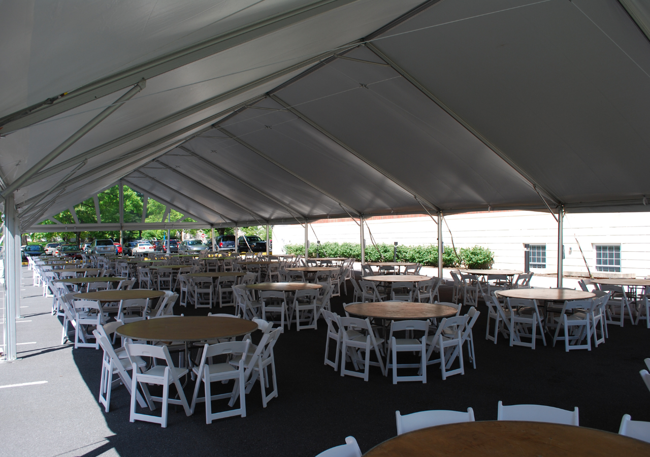corporate_tables_chairs Round tables and white padded folding chairs under a frame tent for an event