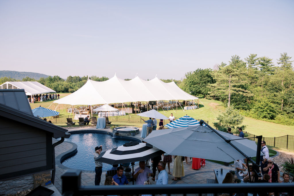 umbrellas set up over outdoor cocktail hour with large white sailcloth style wedding tent in the background under blue sky
