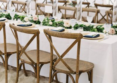 tables set up for seating at long tables with cross-back chairs for beach wedding reception on the sand