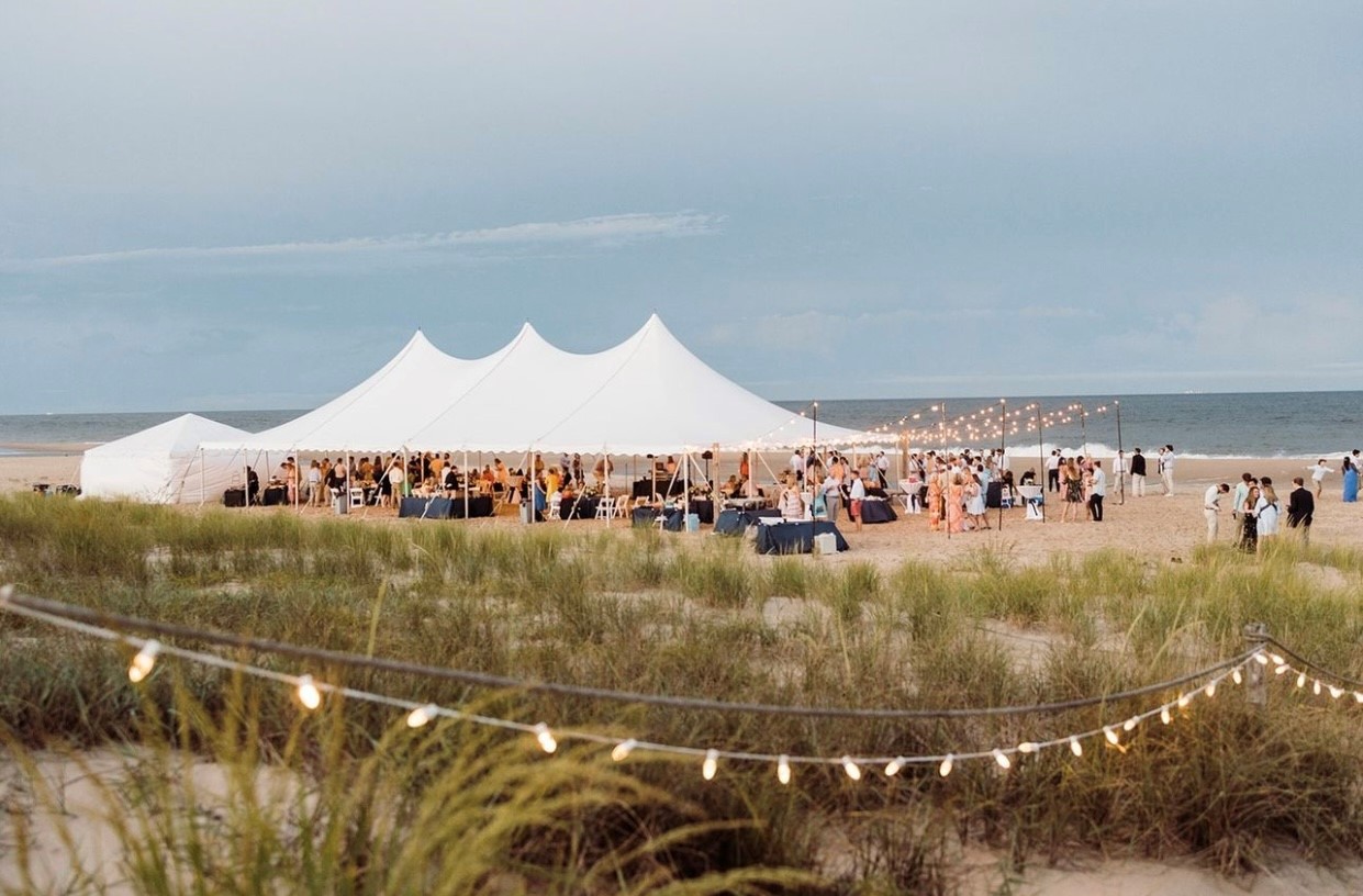 Tented event set up on sandy beach in Delaware with blue skies overhead and ocean as the back drop.