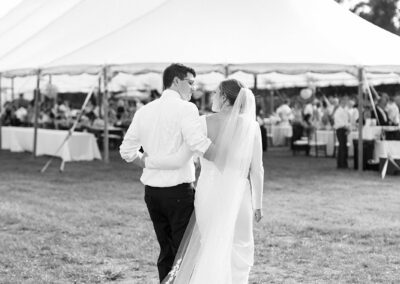 black and white photo of bride and groom walking towards wedding tent
