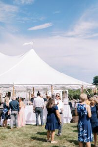 outdoor cocktail hour in grass in front of large wedding tent