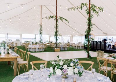 wedding tent interior showing tables for seating, large dance floor, and greenery wrapped center poles.