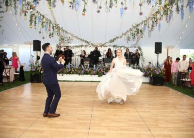 bride and groom dancing on dance floor inside wedding tent draped with flowers
