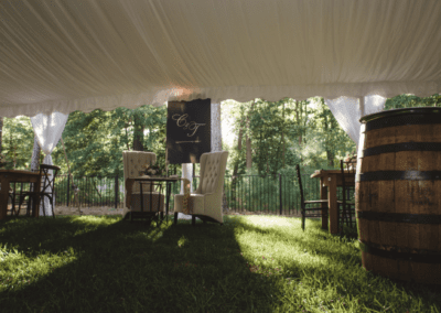 Inside tent view of sweetheart table with white tufted chairs and a wine barrel
