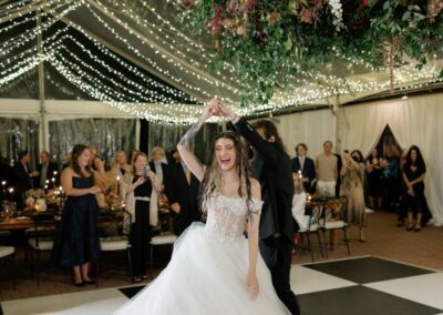 bride and groom dancing on black and white dance floor under wedding tent draped with twinkle lighting