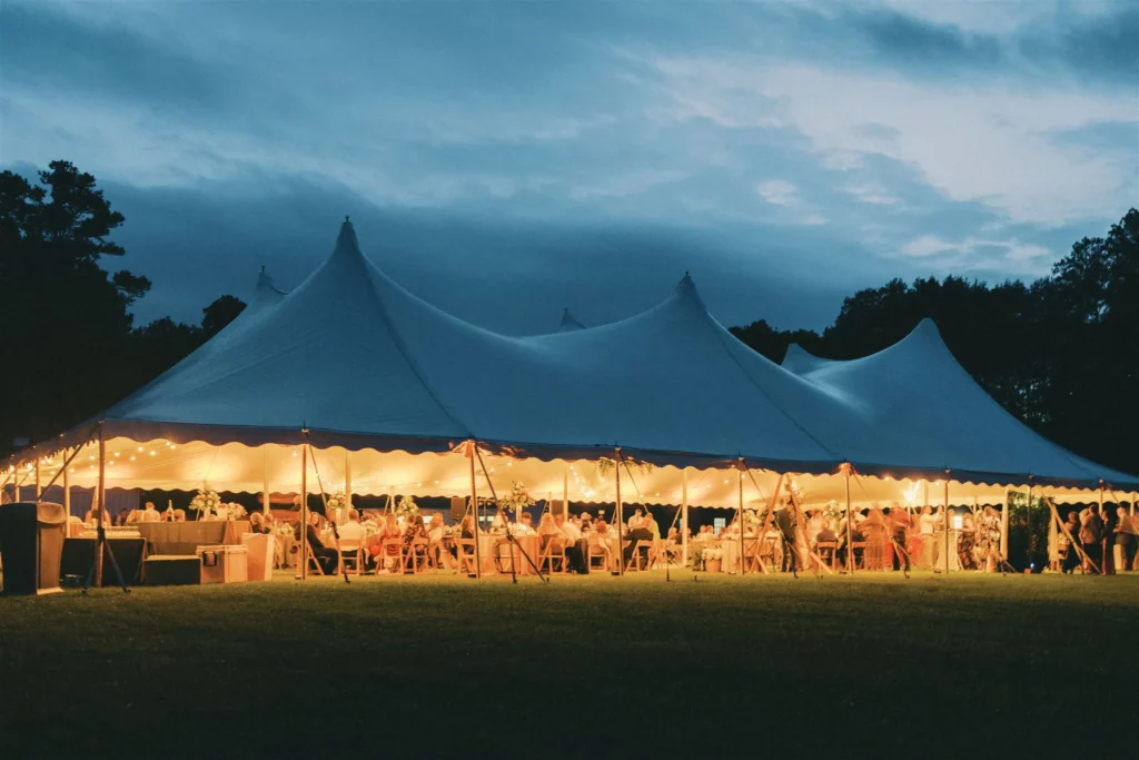 60' by 100' high peak pole tent with interior lighting glow, at dusk.