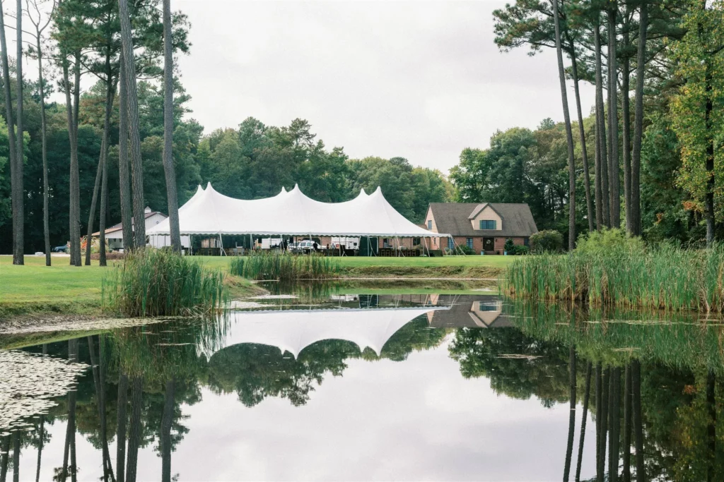 large white wedding tent, installed on grass with reflecting pond in foreground.