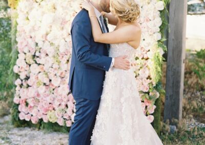 bride and groom standing in front of floral wall at wedding