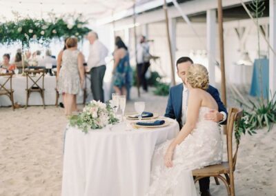 bride and groom at sweet heart table, under a sailcloth wedding tent for beach wedding on the sand