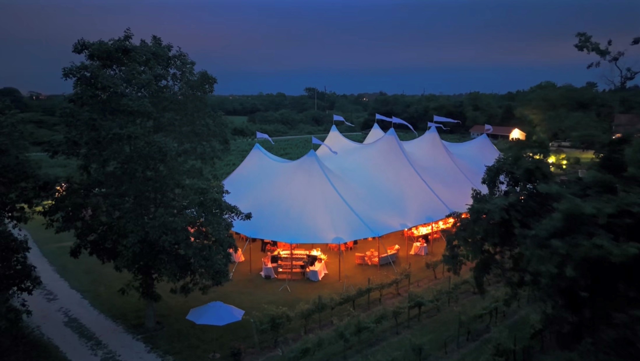 sailcloth style wedding tent photo from drone with tent lighting glowing at dusk