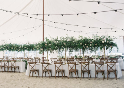 sailcloth tent with lighting wooden crossback chairs set up on sandy beach