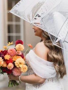 bride carrying clear umbrella and bright floral bouquet
