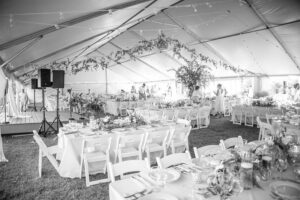 large white tent with greenery draping, and tables and chairs set up underneath.