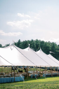 Large white wedding tent set up on lawn with green trees and blue sky in background