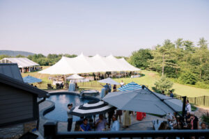 umbrellas set up over outdoor cocktail hour with large white sailcloth style wedding tent in the background under blue sky