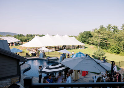umbrellas set up over outdoor cocktail hour with large white sailcloth style wedding tent in the background under blue sky