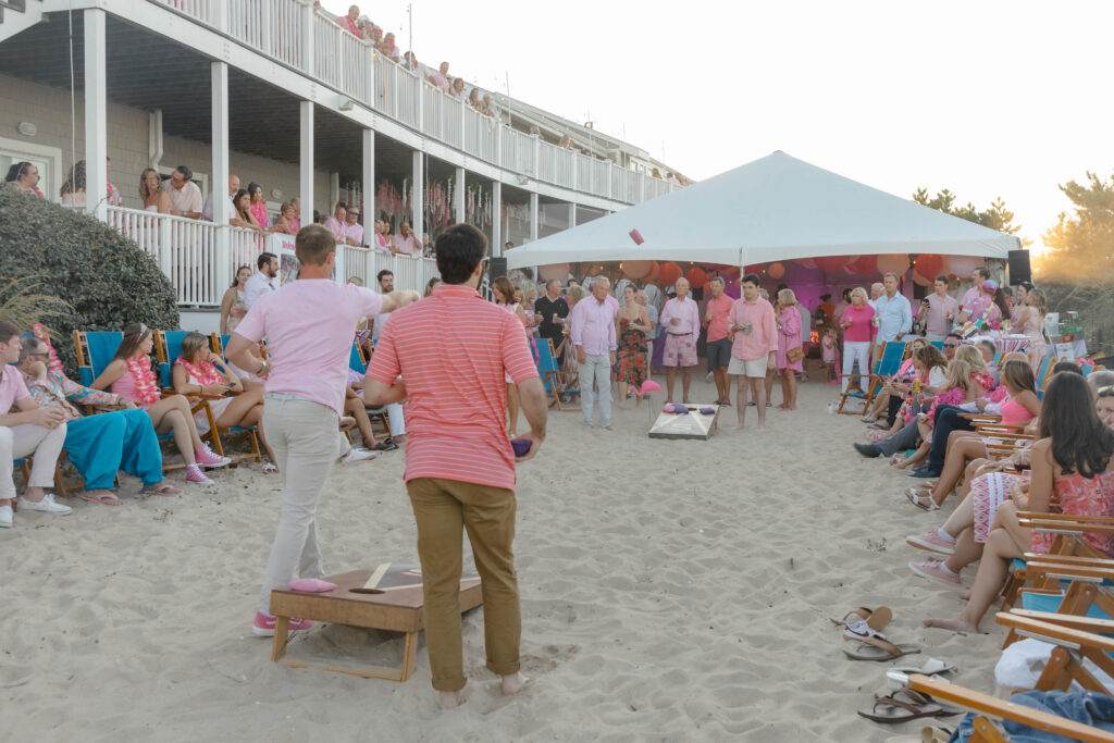 people playing cornhole on the sand at a pink themed party with tent in background