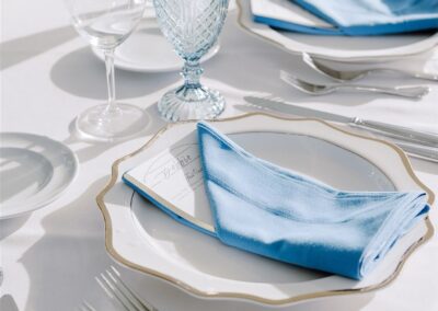 table setting with scalloped white with gold trim isla plate and blue water goblets