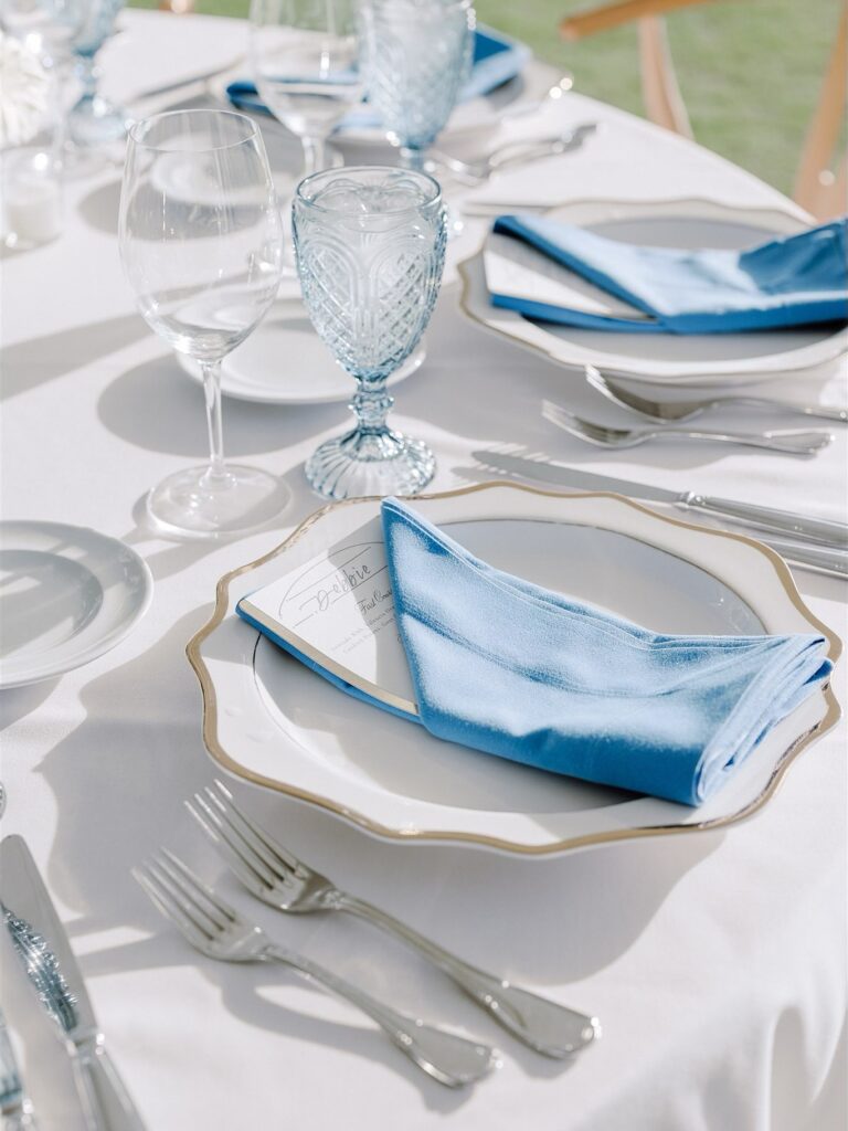 table setting with scalloped white with gold trim isla plate and blue water goblets