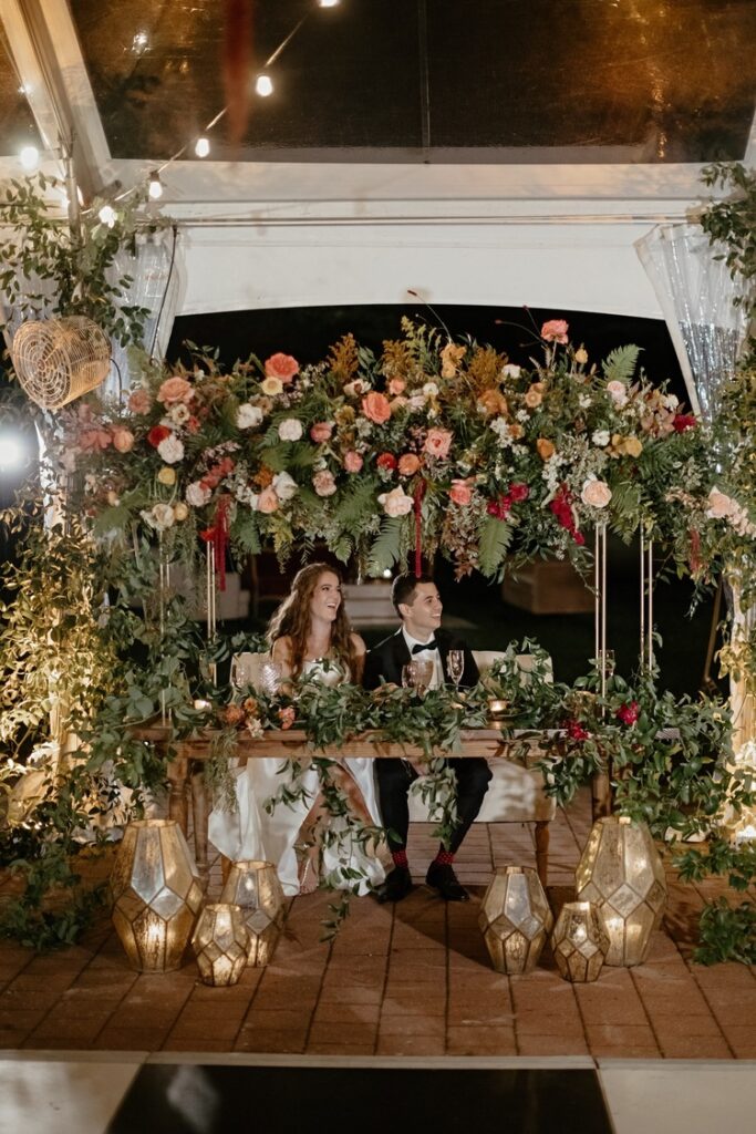 sweet heart table with bride and groom surrounded with lush greenery and bold warm florals.