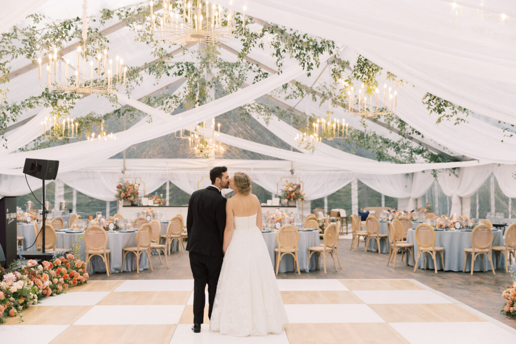 bride and groom standing on birch and white check dance floor under clear top wedding tent
