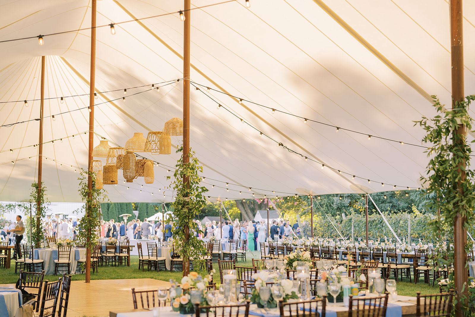 sailcloth wedding tent with greenery wrapping center poles, rattan baskets suspended from ceiling
