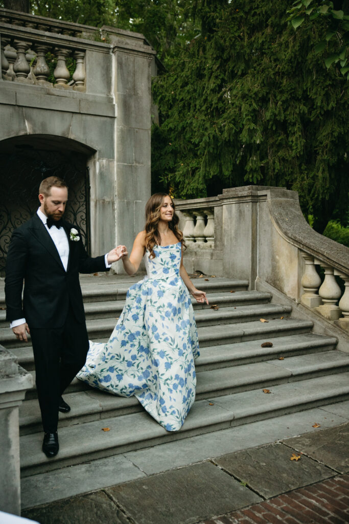 bride wearing blue floral wedding gown walking down steps with groom