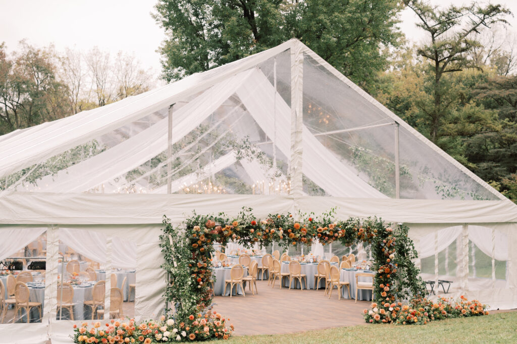 clear top wedding tent with floral archway framing the tent entrance