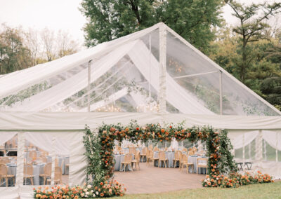 clear top wedding tent with floral archway framing the tent entrance