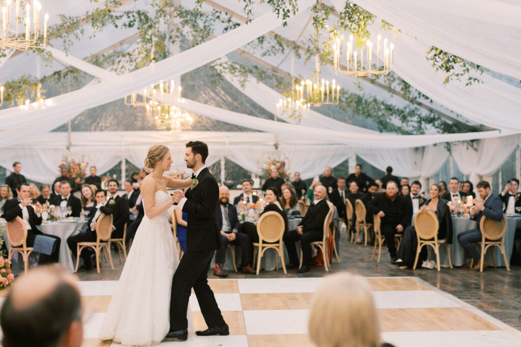 bride and groom dancing on birch and white check dance floor under clear wedding tent