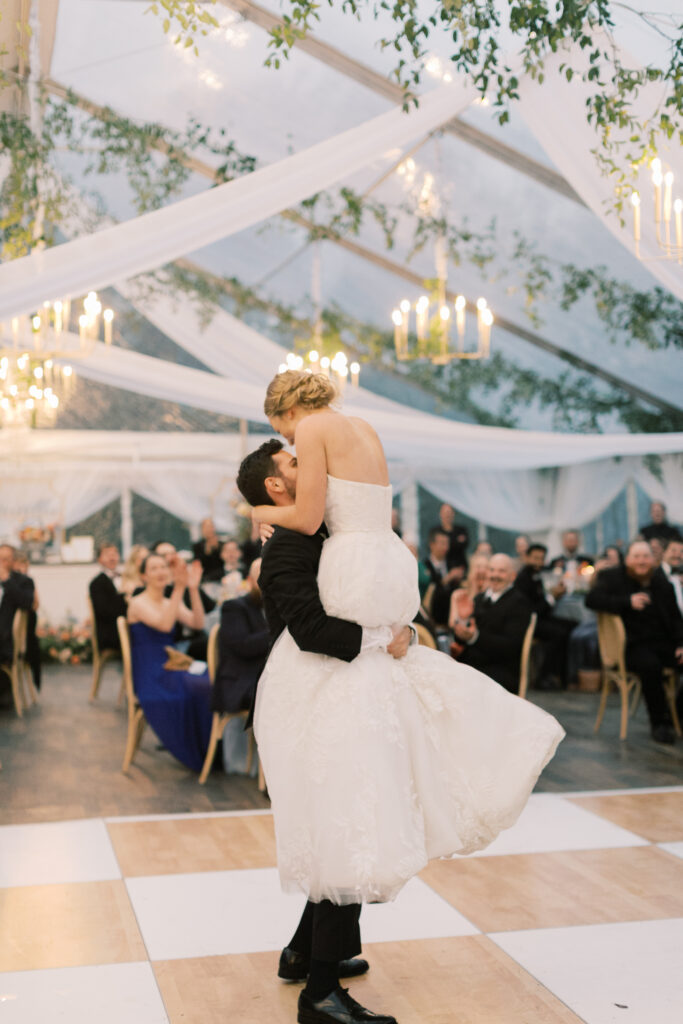 bride and groom dancing on birch and white check dance floor under clear wedding tent
