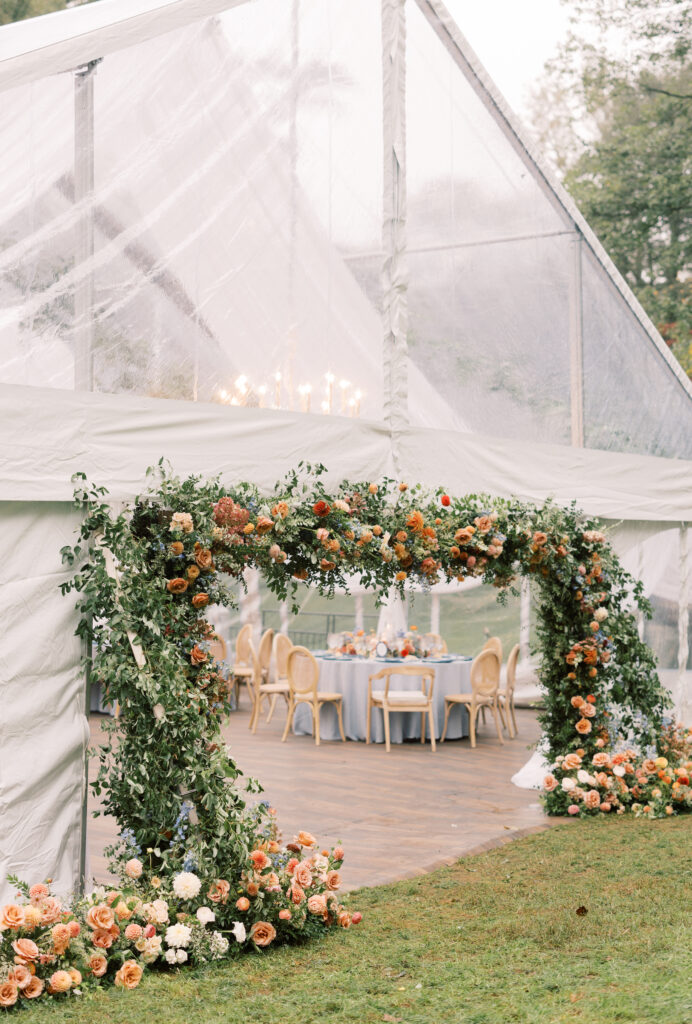 clear top wedding tent with floral archway framing the tent entrance