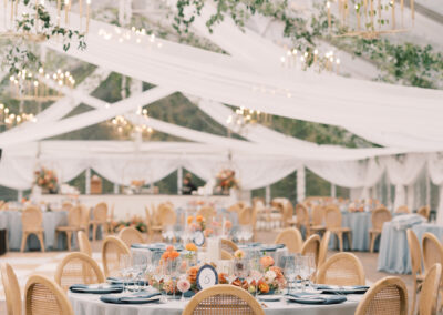 clear top wedding tent with ceiling draping, natural wood chairs, blue table linens