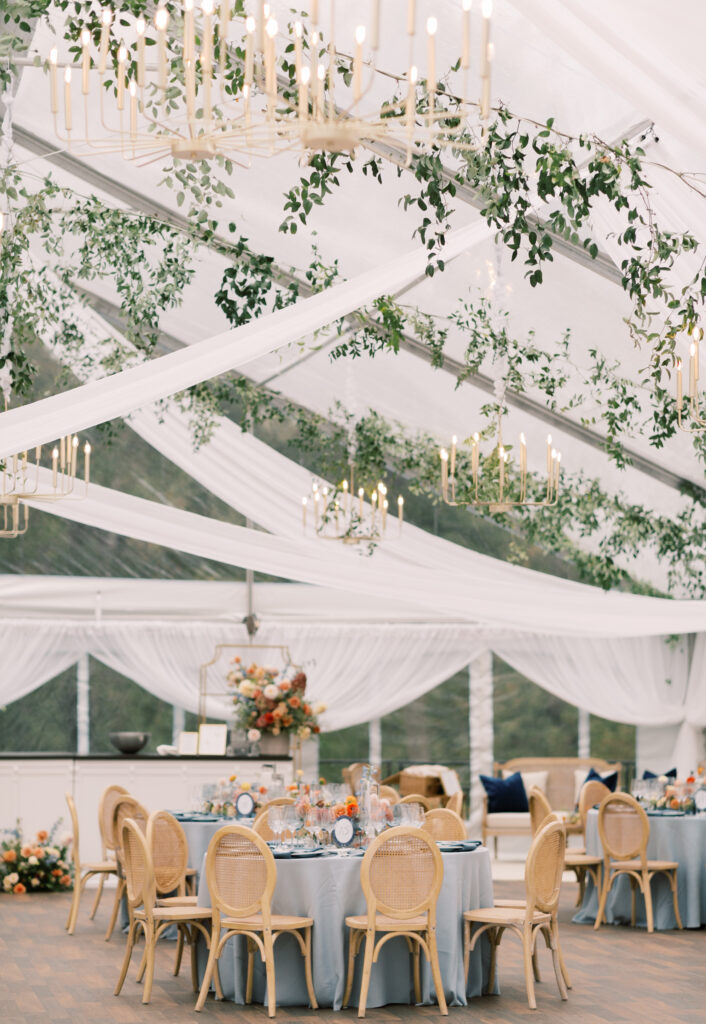 clear top wedding tent with ceiling draping, natural wood chairs, blue table linens