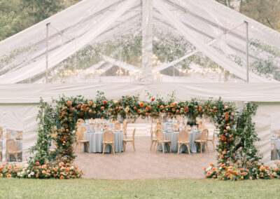 clear top wedding tent with floral archway framing the tent entrance