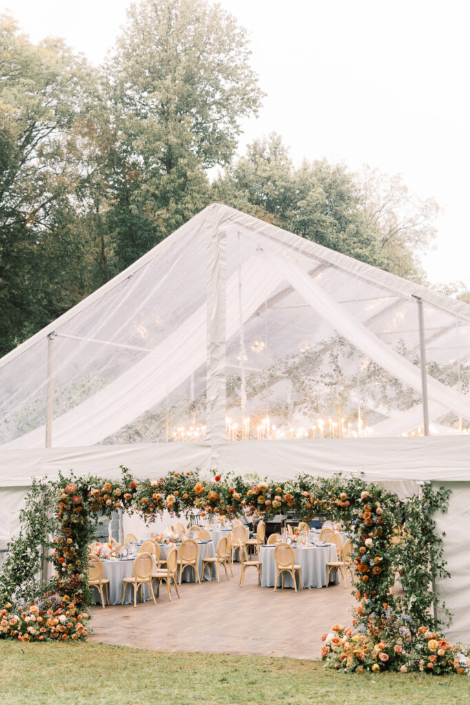 clear top wedding tent with floral archway framing the tent entrance