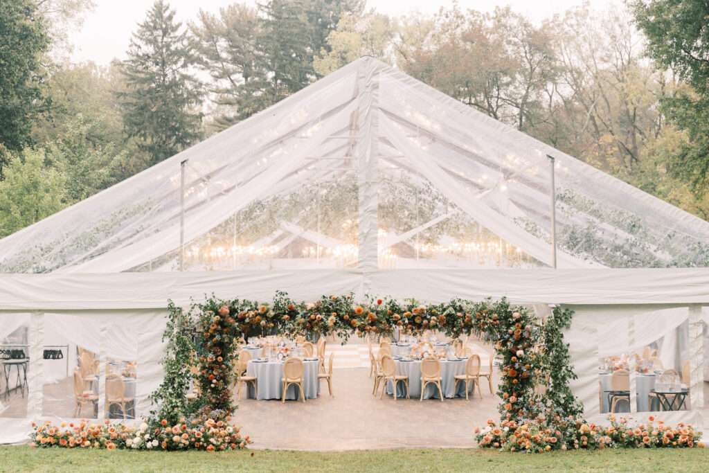 clear top wedding tent with floral archway framing the tent entrance