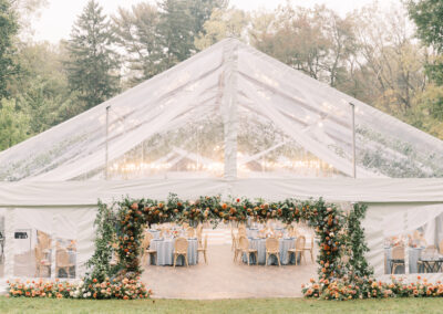 clear top wedding tent with floral archway framing the tent entrance